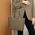 A woman wearing the Cuirae brown genuine leather bag in front of a window with blinds.