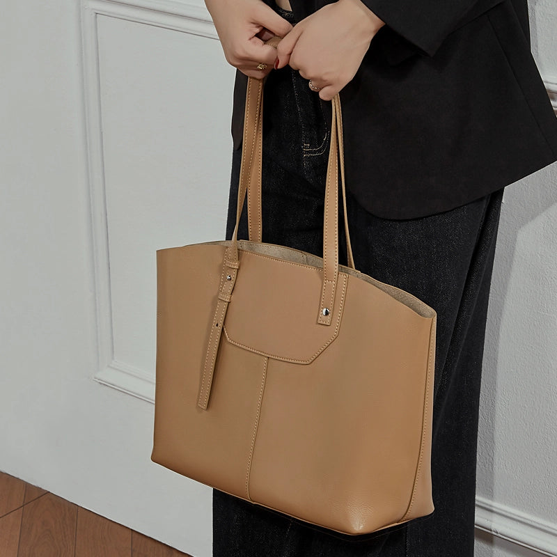 Model stands against the wall with her hands by her sides, holding a Cuirae brown genuine leather bag.