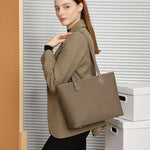 A woman shouldered the Cuirae brown genuine leather bag in front of a window with blinds.