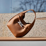 Cuirae brown genuine leather crossbody bag on outdoor stone bench, angled view showing pebbled texture and cross turnlock
