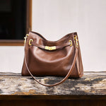 Cuirae brown genuine leather crossbody bag in rustic still life setting, showing hobo silhouette and gold turnlock detail
