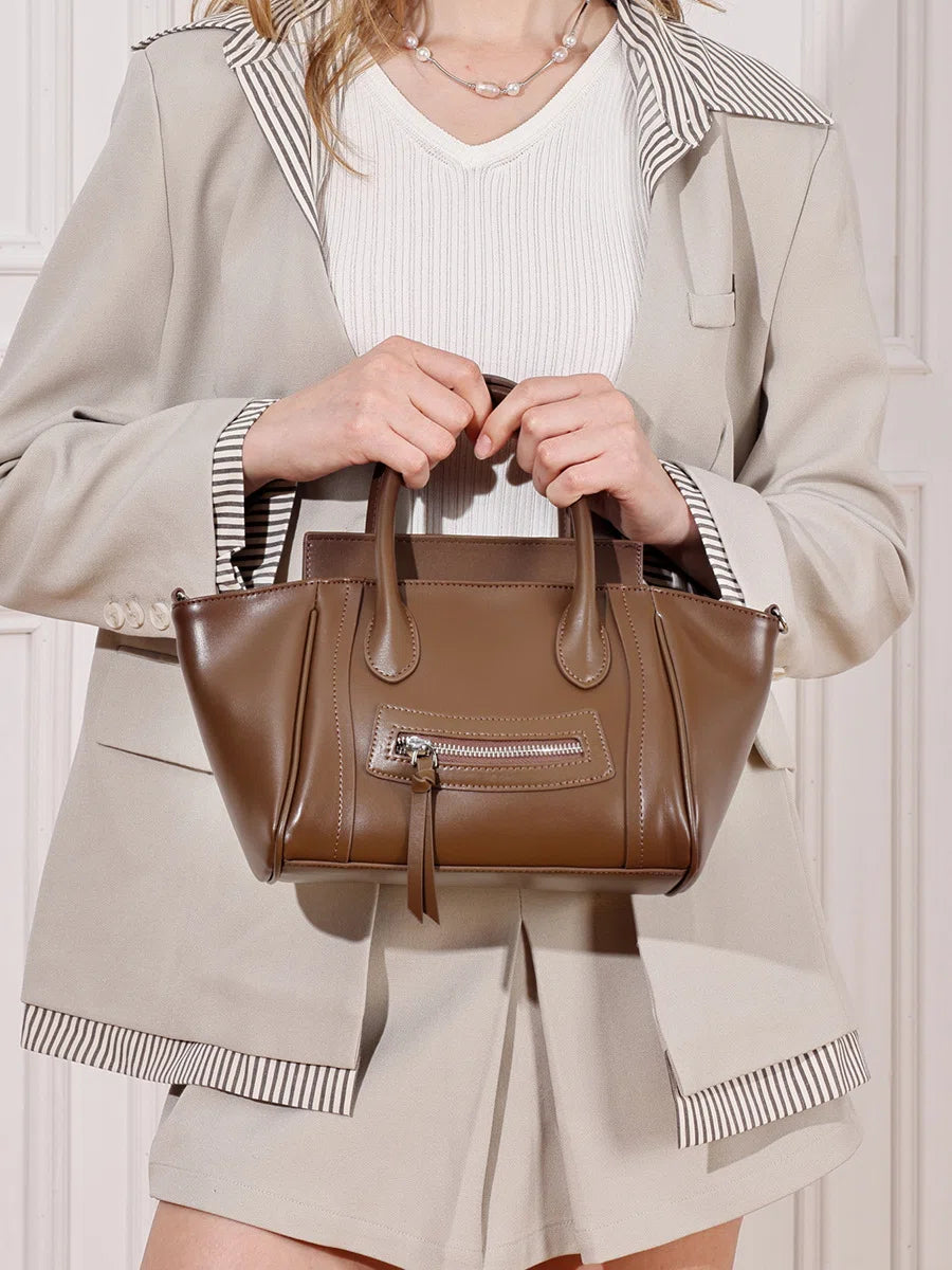 A woman holding the Cuirae brown genuine leather handbag in front of her.