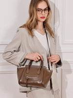 A woman wearing a beige blazer carrying the Cuirae brown genuine leather handbag on her shoulder.