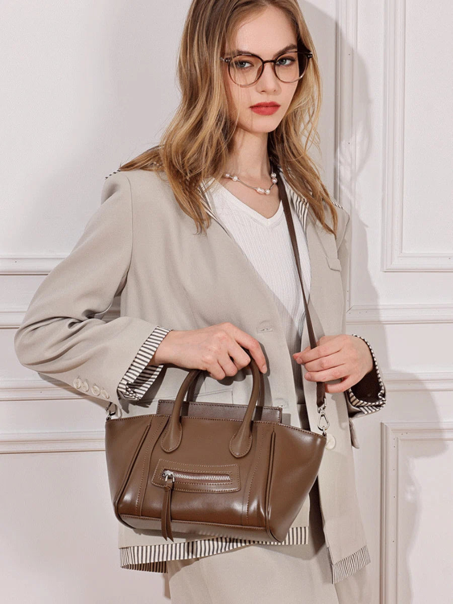 A woman wearing a beige blazer carrying the Cuirae brown genuine leather handbag on her shoulder.