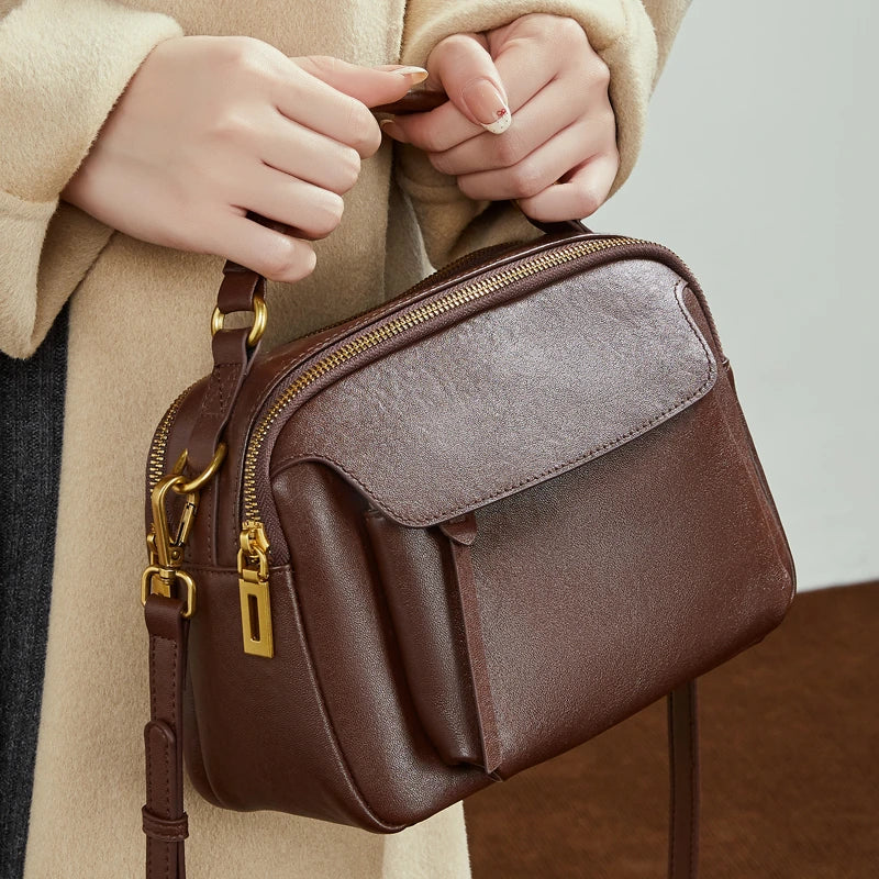 Model holding Cuirae  brown genuine leather shoulder bag, closeup showing antique gold hardware and front pocket