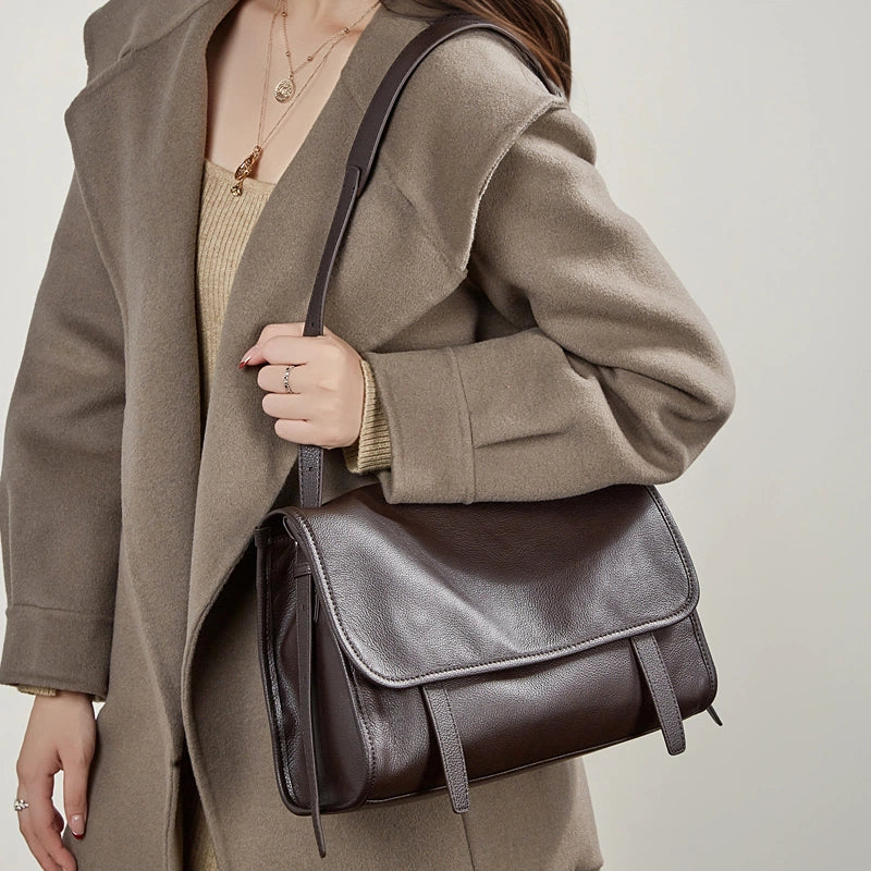 Woman wearing Cuirae brown leather shoulder bag, front view showing flap closure and adjustable strap