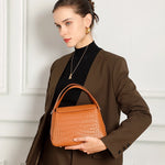 Model holding Cuirae brown leather crossbody bag, front view showcasing crocodile texture and structured silhouette
