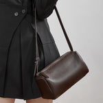 Woman wearing Cuirae brown leather crossbody bag on shoulder, side view showing barrel silhouette and pebbled texture