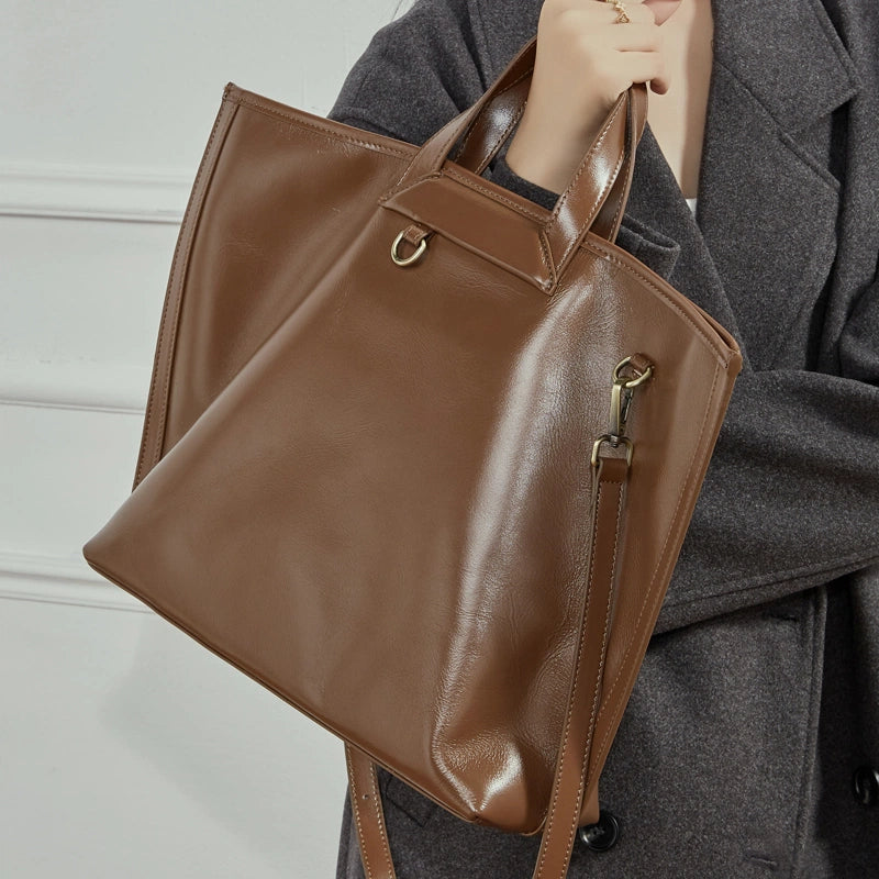 Model holding Cuirae brown genuine leather tote bag with top handles, showing adjustable crossbody strap, side view