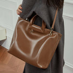 Model wearing Cuirae brown genuine leather tote bag on shoulder, angled view highlighting soft genuine leather texture