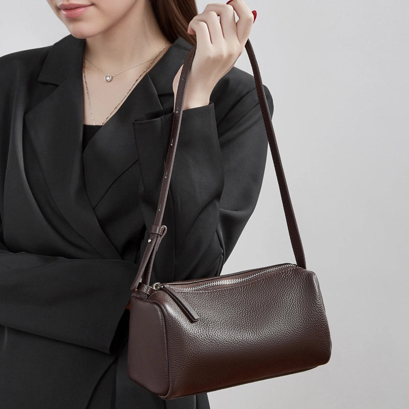 Model holding Cuirae brown pebbled genuine leather barrel crossbody bag, closeup showing adjustable strap and zipper detail