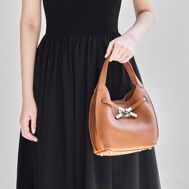 Model holding Cuirae brown pebbled leather hobo crossbody bag by top handle, front view showing silver cross turnlock