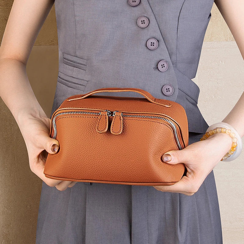 Cuirae brown pebbled genuine leather makeup bag with top handle, wrist carry held by model in angled view