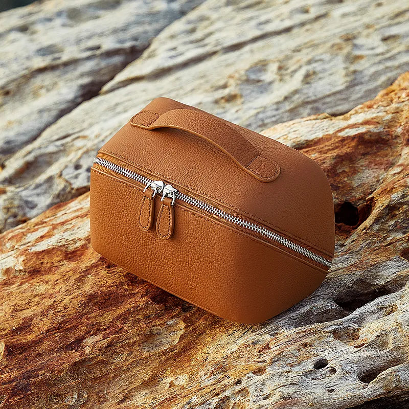 Cuirae brown pebbled genuine leather makeup bag with double zipper and top handle, outdoor still life on rock in natural light