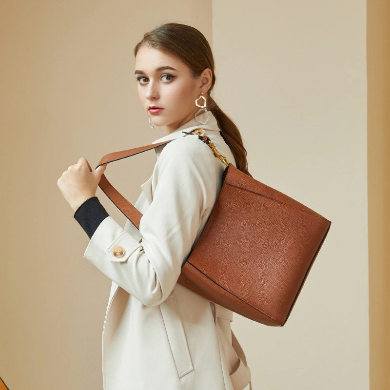 Woman wearing Cuirae brown pebbled leather bucket bag on shoulder, side view with hand holding the strap
