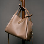 Cuirae brown pebbled genuine leather handbag hanging on wooden rack, angled view showing gold zipper hardware