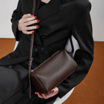 Model sitting holding Cuirae  brown pebbled leather crossbody bag, warm indoor scene showing versatile styling