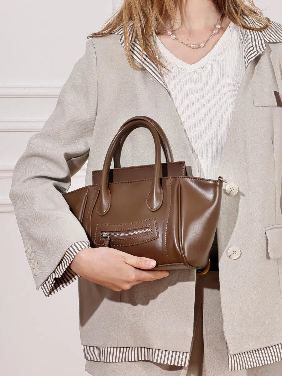 A woman carrying the Cuirae brown top grain cowhide handbag against her side.