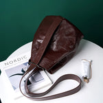 Cuirae burgundy glossy crinkled leather bucket bag on white round table, still life showing wide adjustable shoulder strap