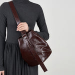 Model wearing Cuirae burgundy leather bucket bag crossbody, hand resting on strap with dark grey turtleneck dress outfit
