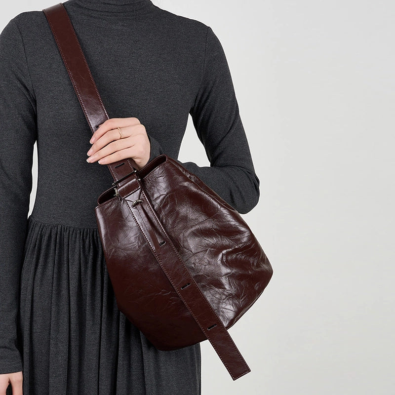 Model wearing Cuirae burgundy leather bucket bag crossbody, hand resting on strap with dark grey turtleneck dress outfit
