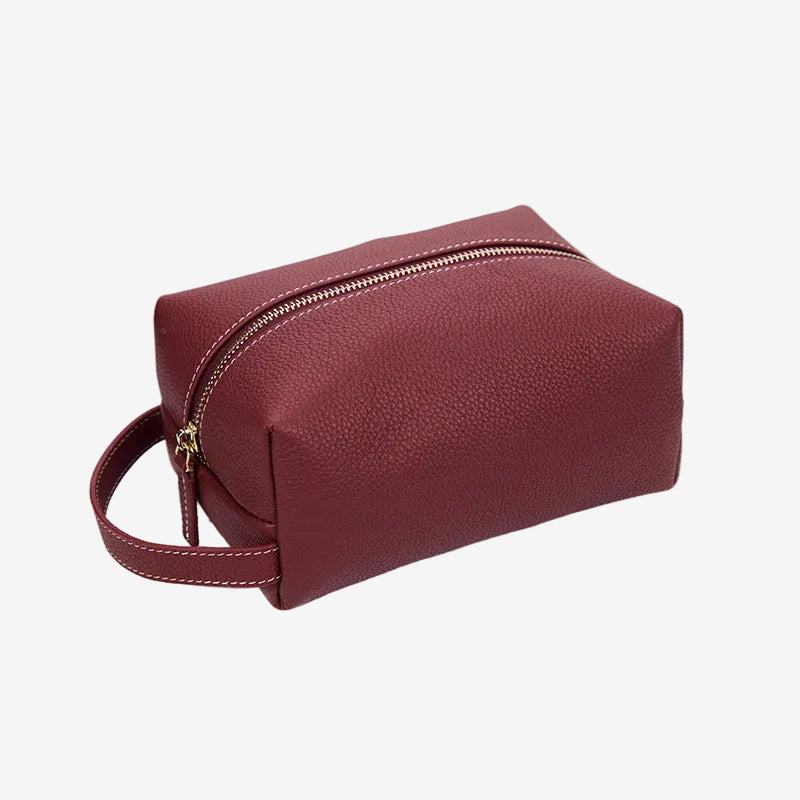 Cuirae burgundy pebbled genuine leather makeup bag with gold zipper and wrist strap, front angled view on white background