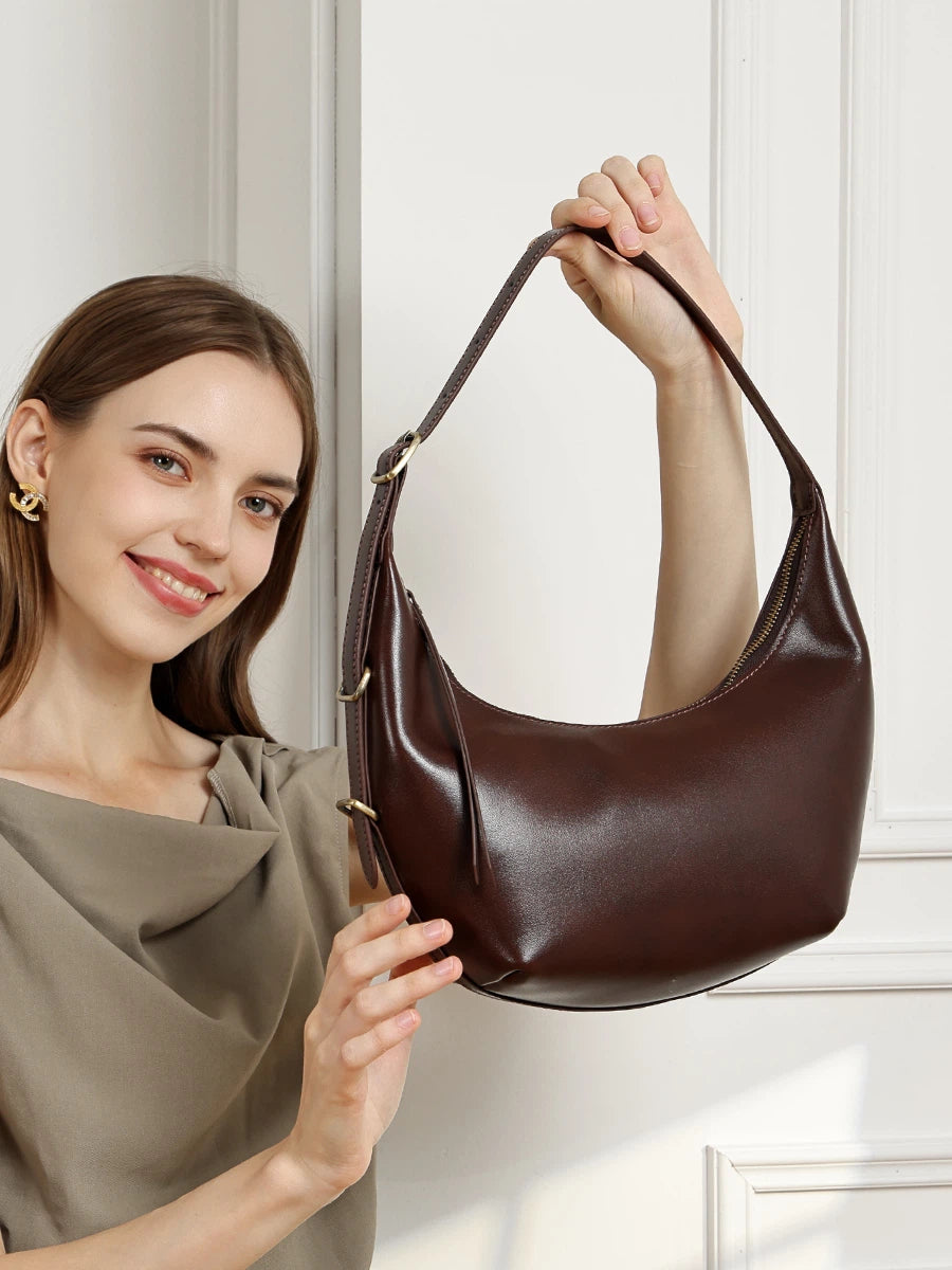 A smiling woman holding up the Cuirae chocolate top grain cowhide handbag with both hands.