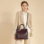 A woman wearing the Cuirae coffee genuine leather tote bag  across her body against a beige background