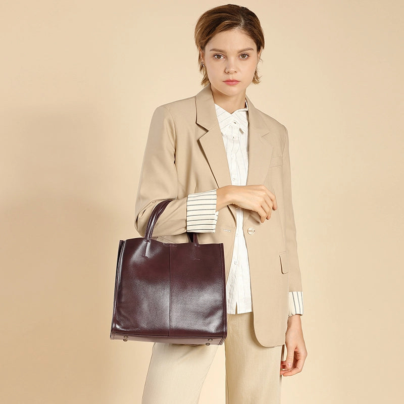 A woman handles the Cuirae coffee genuine leather tote bag  against a beige background
