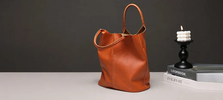 A soft brown Cuirae 100% real leather tote bag on a desk next to a candle. We are always here to help you.
