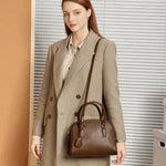 Woman wearing Cuirae dark brown genuine  leather dome handbag on shoulder, front view showing structured silhouette and tag charm