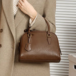 Cuirae dark brown genuine leather handbag carried on arm, closeup showing smooth leather texture and gold hardware
