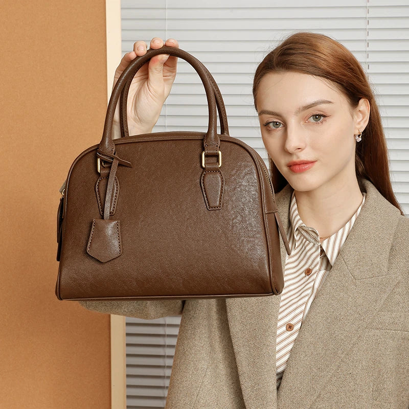 Model holding Cuirae dark brown genuine leather handbag by top handle, front view showing classic dome design

