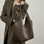 A model in a green jacket holding the Cuirae coffee genuine leather tote bag.