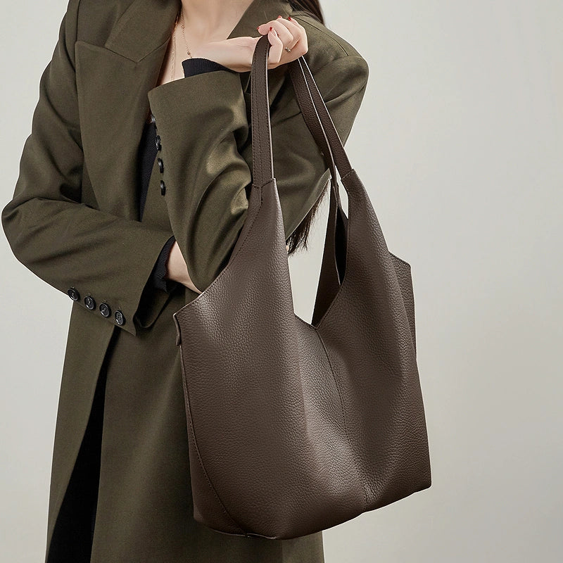 A model in a green jacket holding the Cuirae coffee genuine leather tote bag.