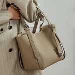 Woman wearing Cuirae gray genuine leather bucket bag on shoulder, side view with striped blazer outfit