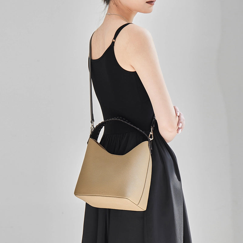 Model wearing Cuirae gray leather bucket bag on shoulder, back view with black sleeveless dress outfit