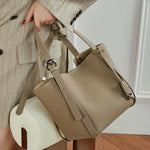 Model holding Cuirae gray pebbled leather bucket bag by handle, angled view showing adjustable strap and silver hardware