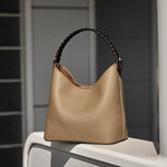 Cuirae gray pebbled leather bucket bag on white windowsill, natural light showing black braided top handle