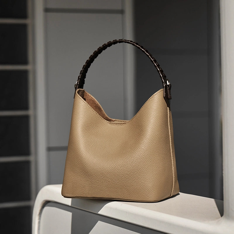 Cuirae gray pebbled leather bucket bag on white windowsill, natural light showing black braided top handle