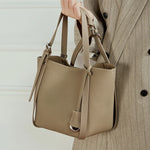 Model holding Cuirae gray pebbled leather bucket bag by handle, front view showcasing silver hardware details