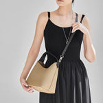 Woman wearing Cuirae gray pebbled leather bucket bag crossbody, front view with hand holding the bag bottom
