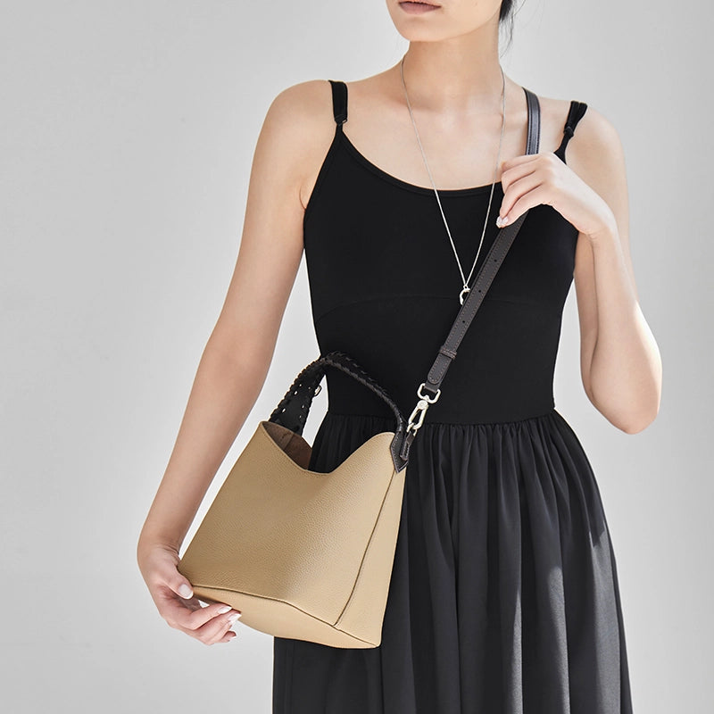 Woman wearing Cuirae gray pebbled leather bucket bag crossbody, front view with hand holding the bag bottom