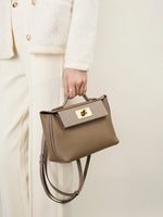 Model holding Cuirae gray pebbled leather flap kelly crossbody bag, front view with white monochrome outfit