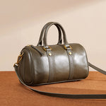 Cuirae green genuine leather barrel crossbody bag on warm surface, showing smooth texture and gold hardware