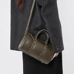 Woman wearing Cuirae green leather barrel crossbody bag, angled view showing versatile styling options