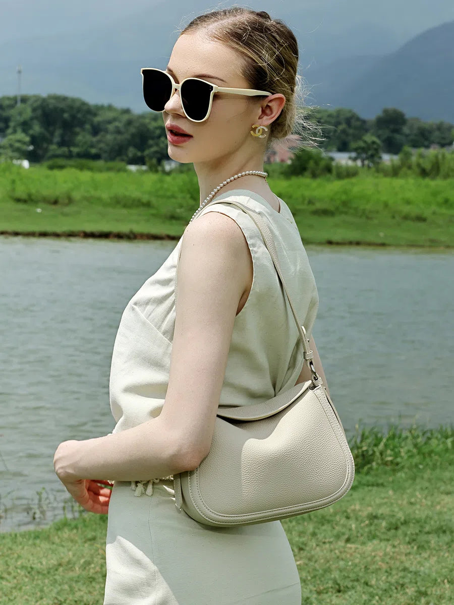 Model wearing a Cuirae ivory pebbled leather shoulder bag at her side by the river.