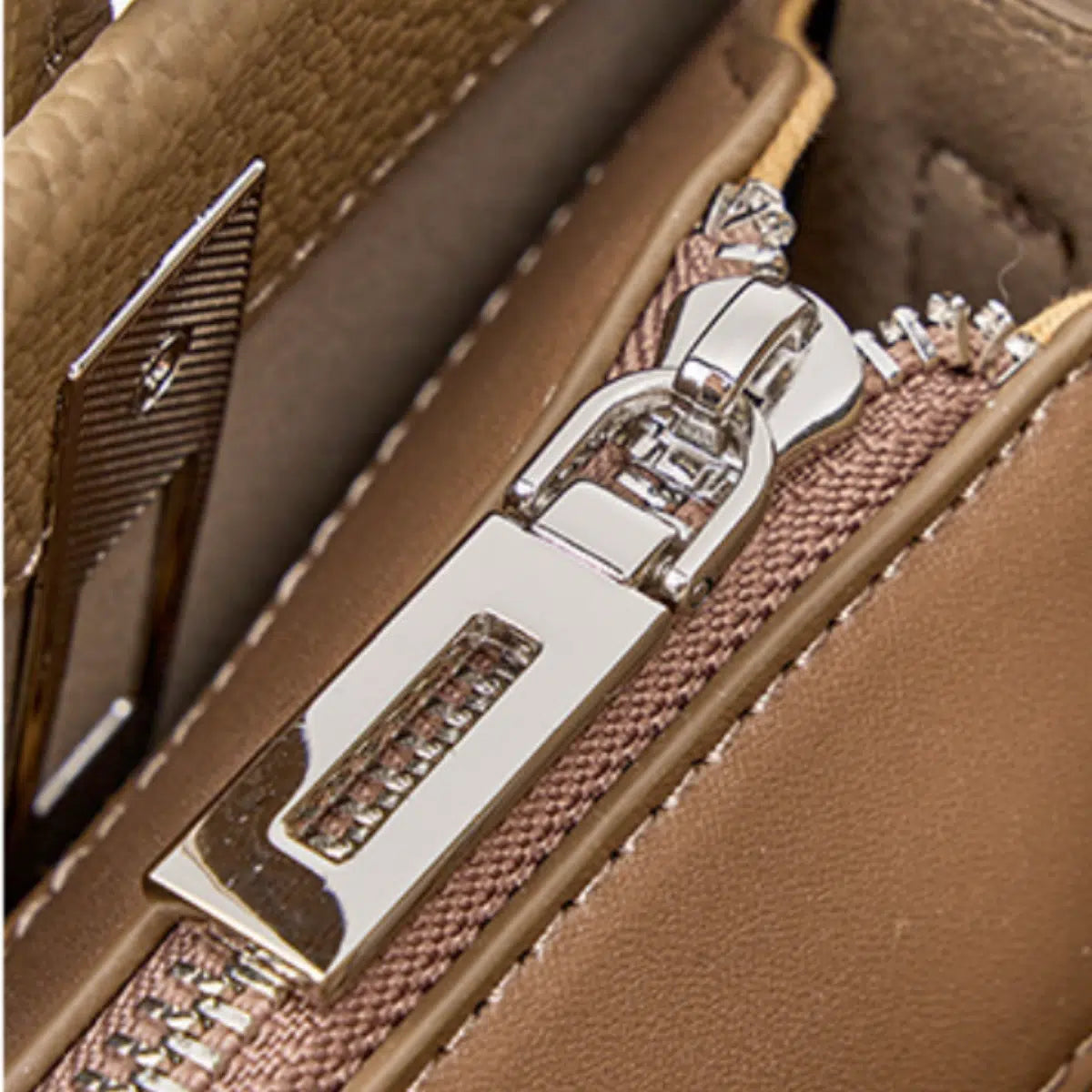 Close-up of the silver-tone zipper and stitched leather trim on a taupe tote