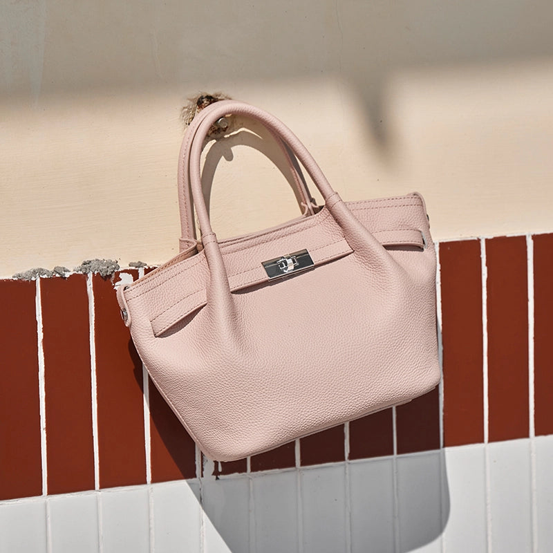 Cuirae light pink leather kelly crossbody bag on outdoor tile wall, angled view showing pebbled texture and structured shape