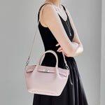 Woman wearing Cuirae light pink genuine leather crossbody bag on shoulder, side view showcasing top handle and silver hardware